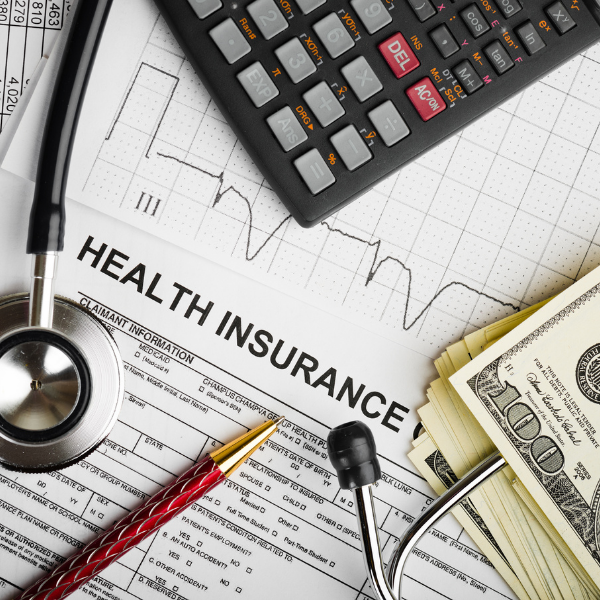 desk covered with calculator, graph, stethoscope, and hundred dollar bills