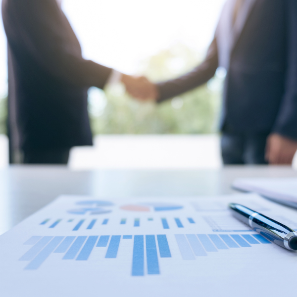 two people shaking hands in front of a graph on a table in the foreground